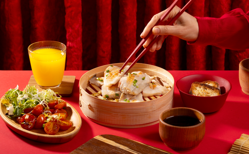 A man’s hands picking up food with chopsticks with red background