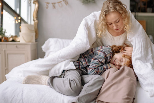 Mother and child cuddling on bed under a white down duvet