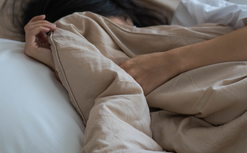 A girl covering her face with a blanket while sleeping
