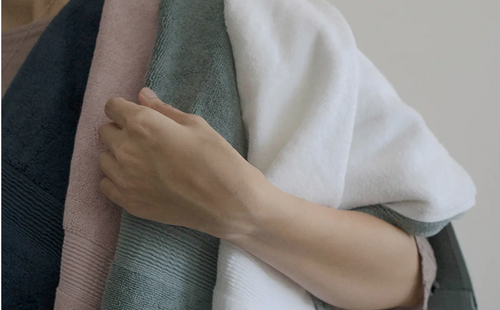 A person placing three bath towels on their shoulders