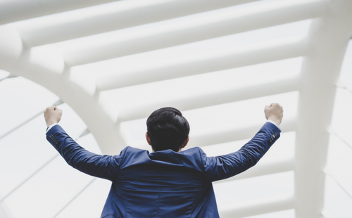 Successfully of young businessman keeping arms raised and expressing positivity while standing outdoors