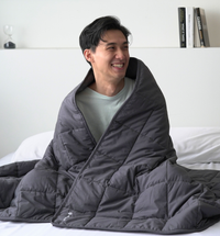 man wrapped in a weighted blanket sitting on bed while smiling