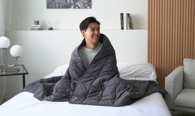 man wrapped in a weighted blanket sitting on bed while smiling