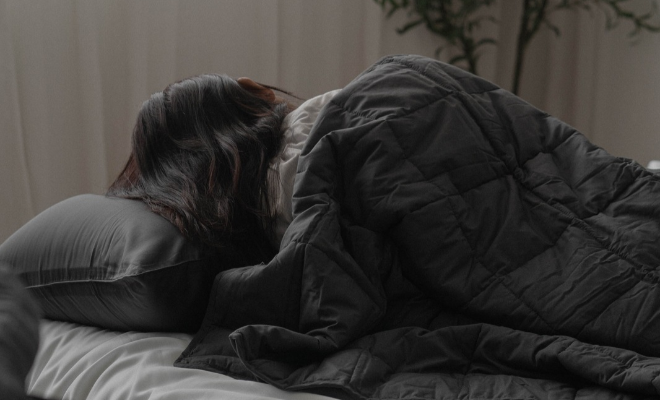 woman sleeping under a black weighted blanket with her back facing the camera